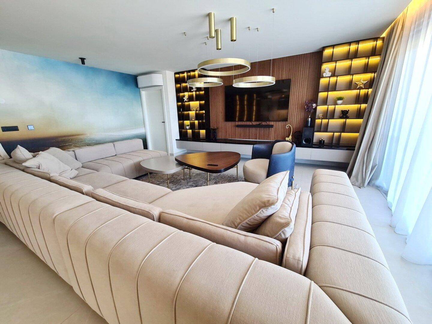 Geräumiges Wohnzimmer mit großem beigem Ecksofa, moderner Einrichtung und Blick auf das Meer.