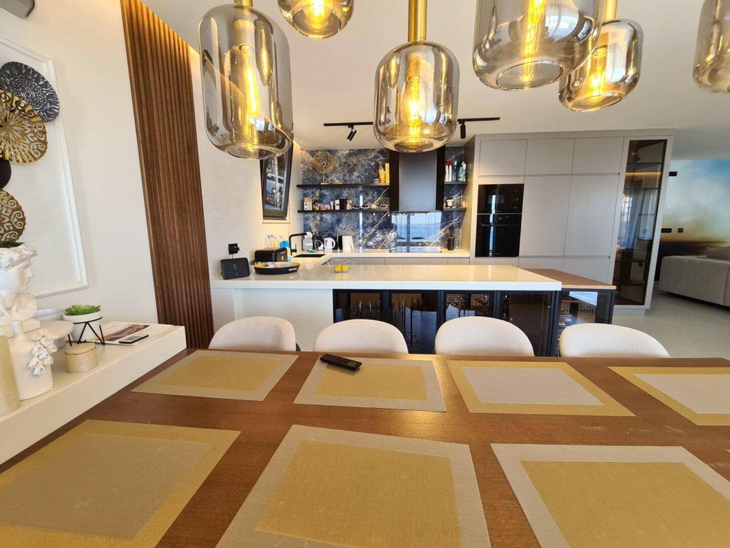 Offene Küche mit Essbereich, modernen Hängelampen und hochwertigen Geräten in stilvollem Design.