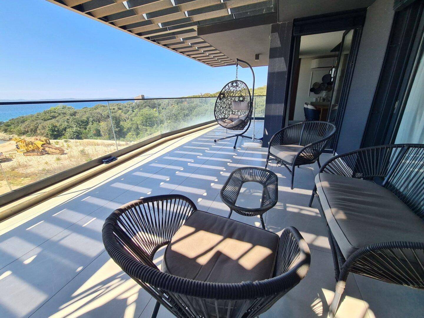 Sonniger Balkon mit modernen Outdoor-Möbeln und weitem Blick auf das Meer und die Umgebung.