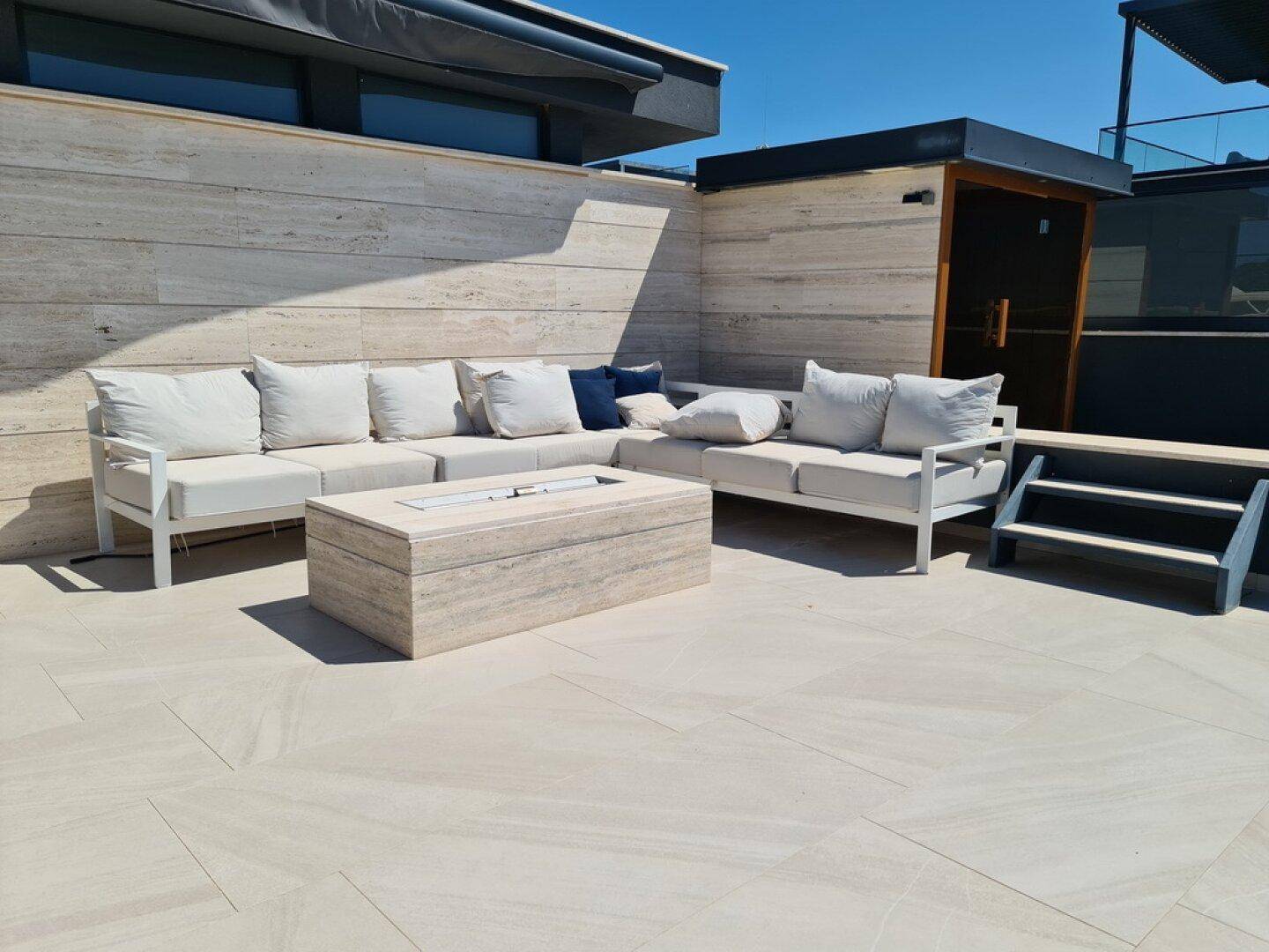Dachterrasse mit luxuriösen Lounge-Möbeln, einem Feuerstellen-Tisch und hellem Fliesenboden.