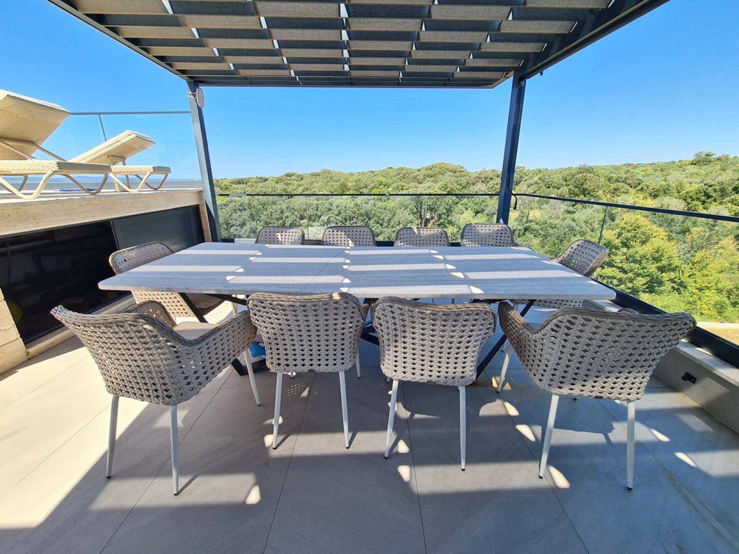 Dachterrasse mit großem Esstisch, Sonnenliegen und weitem Blick ins Grüne und auf das Meer.