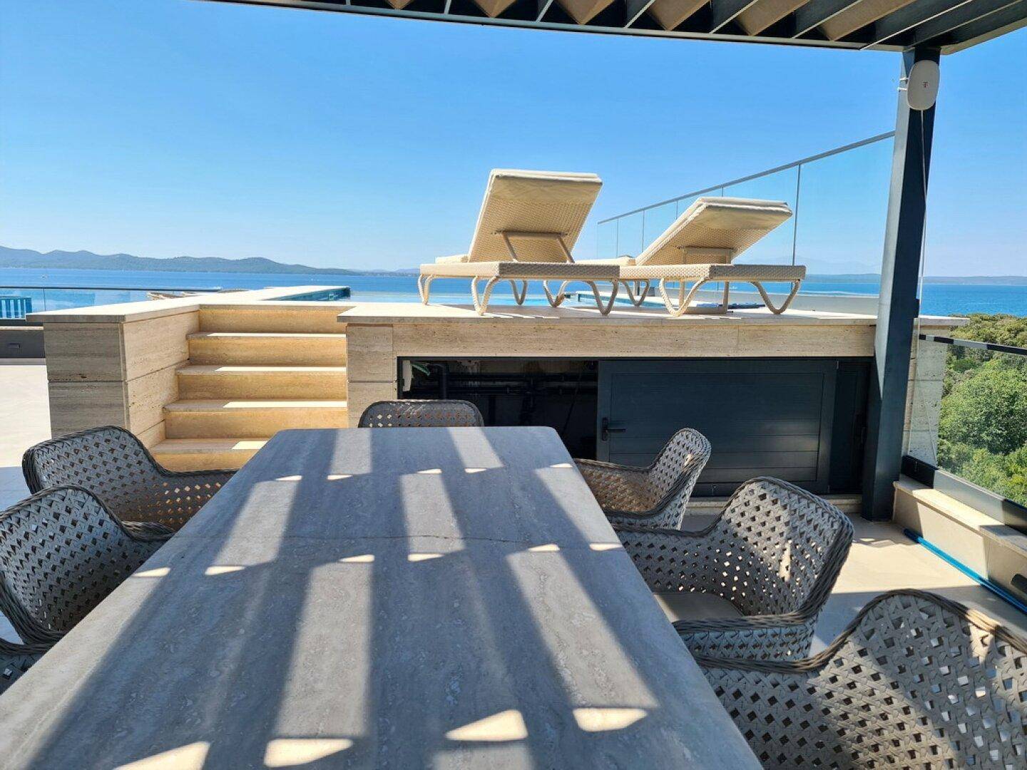 Dachterrasse mit Essbereich, Sonnenliegen und Zugang zum Poolbereich mit Meerblick.