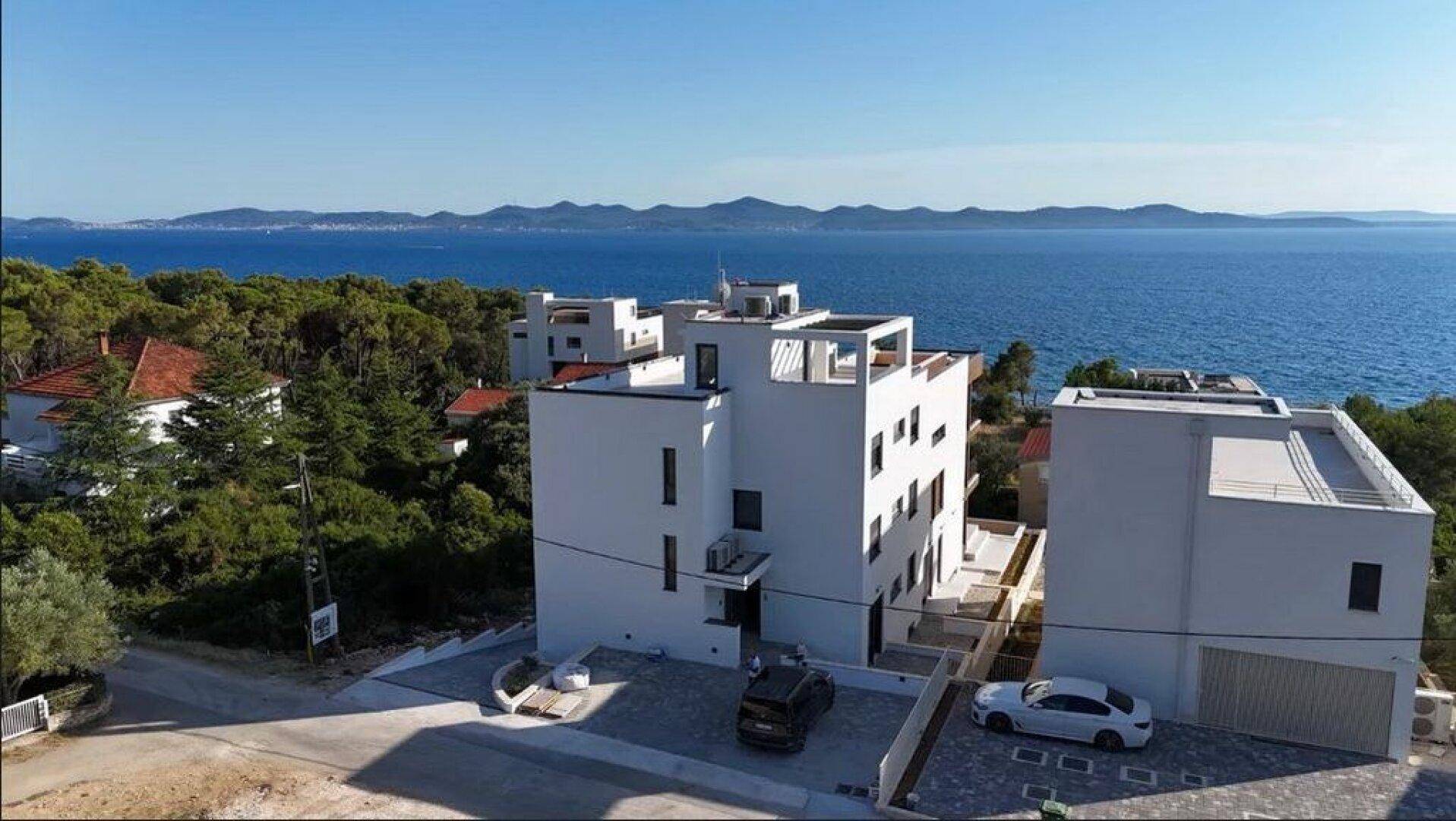 Luftaufnahme der modernen Wohnanlage mit Parkplätzen und weitem Blick über das Meer und die Küste.