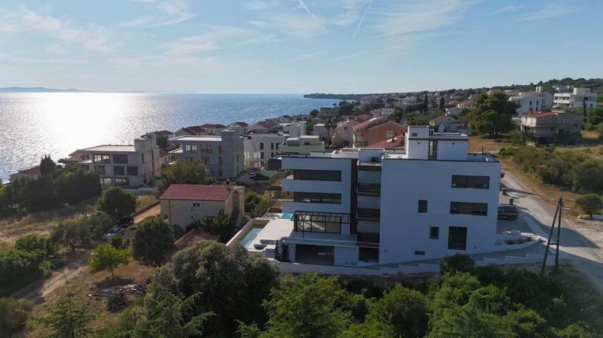 Panoramablick auf die moderne Wohnanlage mit Meerblick und grünen Hügeln.