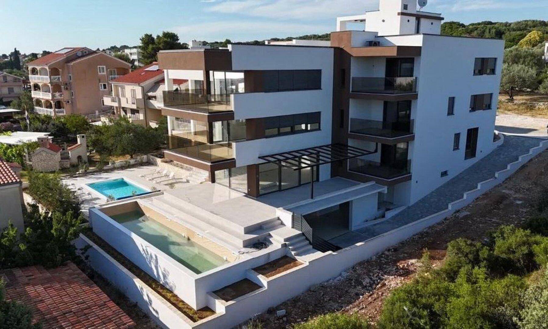 Moderne Wohnanlage mit mehreren Pools und Terrassen bei Sonnenuntergang.