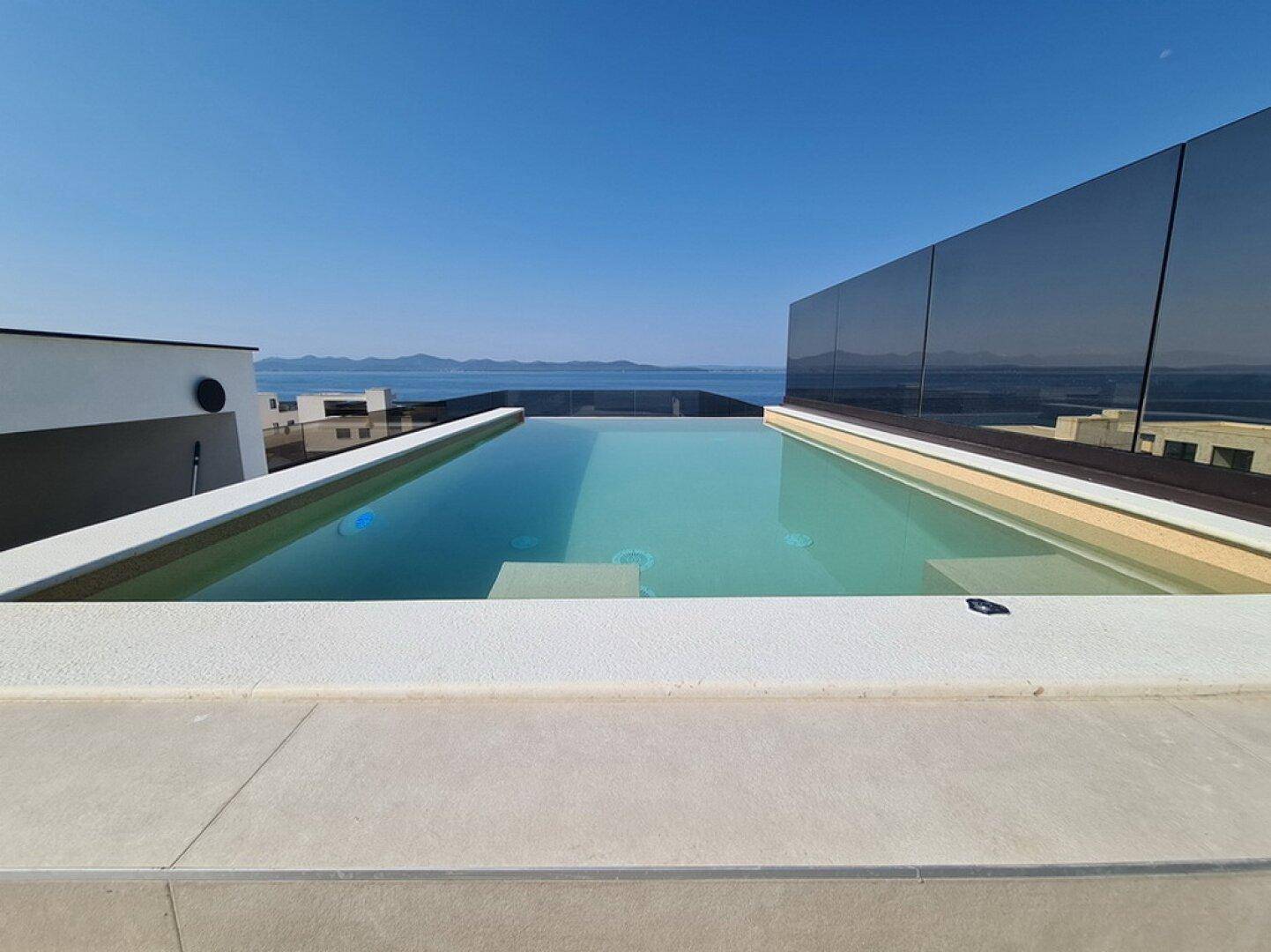 Dachterrasse mit Infinity-Pool und atemberaubendem Meerblick unter klarem Himmel.