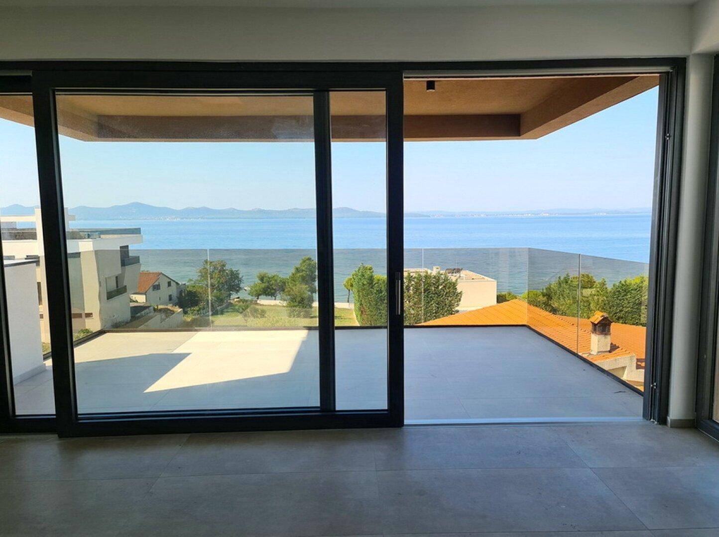 Innenraum mit großen Glasfronten und weitem Meerblick, der viel Tageslicht hereinlässt.