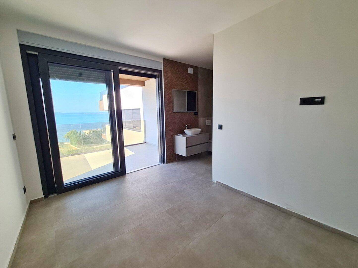 Schlafzimmer mit Zugang zum Balkon und angrenzendem modernen Badbereich mit Waschtisch.
