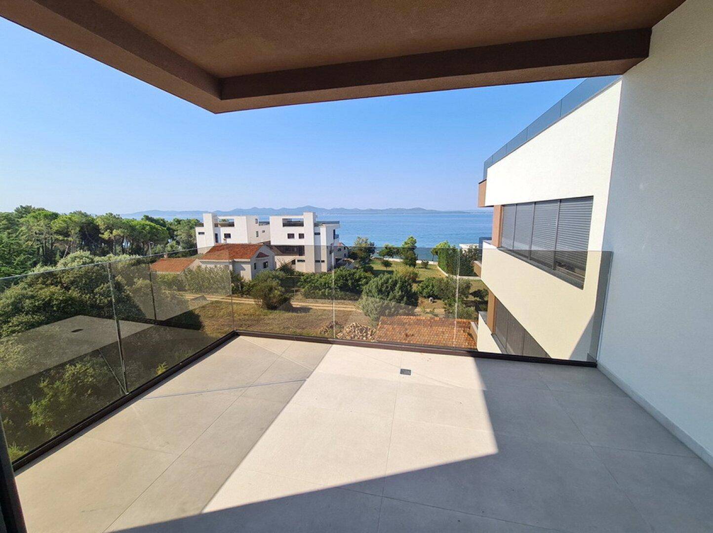 Geräumiger Balkon mit Glasgeländer und weitem Blick auf das glitzernde Meer.