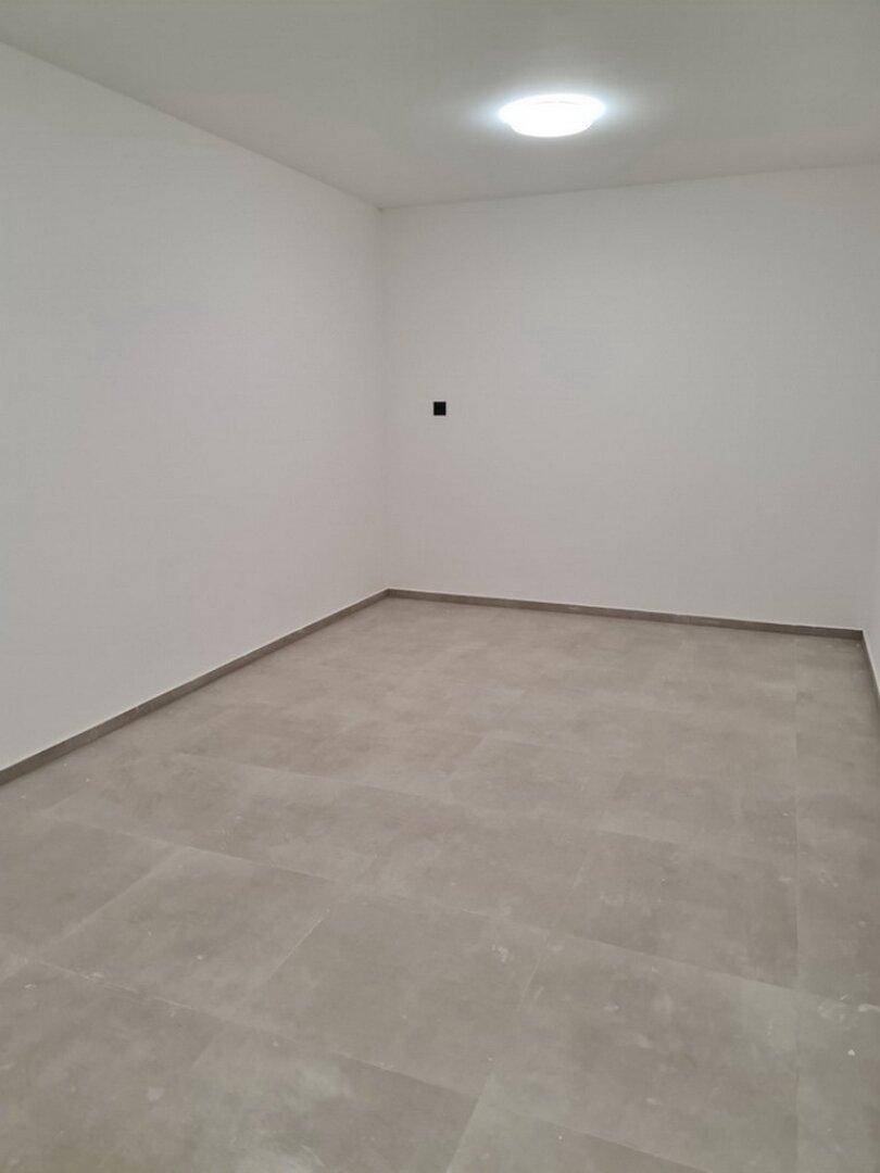 Leerer Raum mit schlichten weißen Wänden und einer Deckenleuchte, ideal für verschiedene Nutzungen.