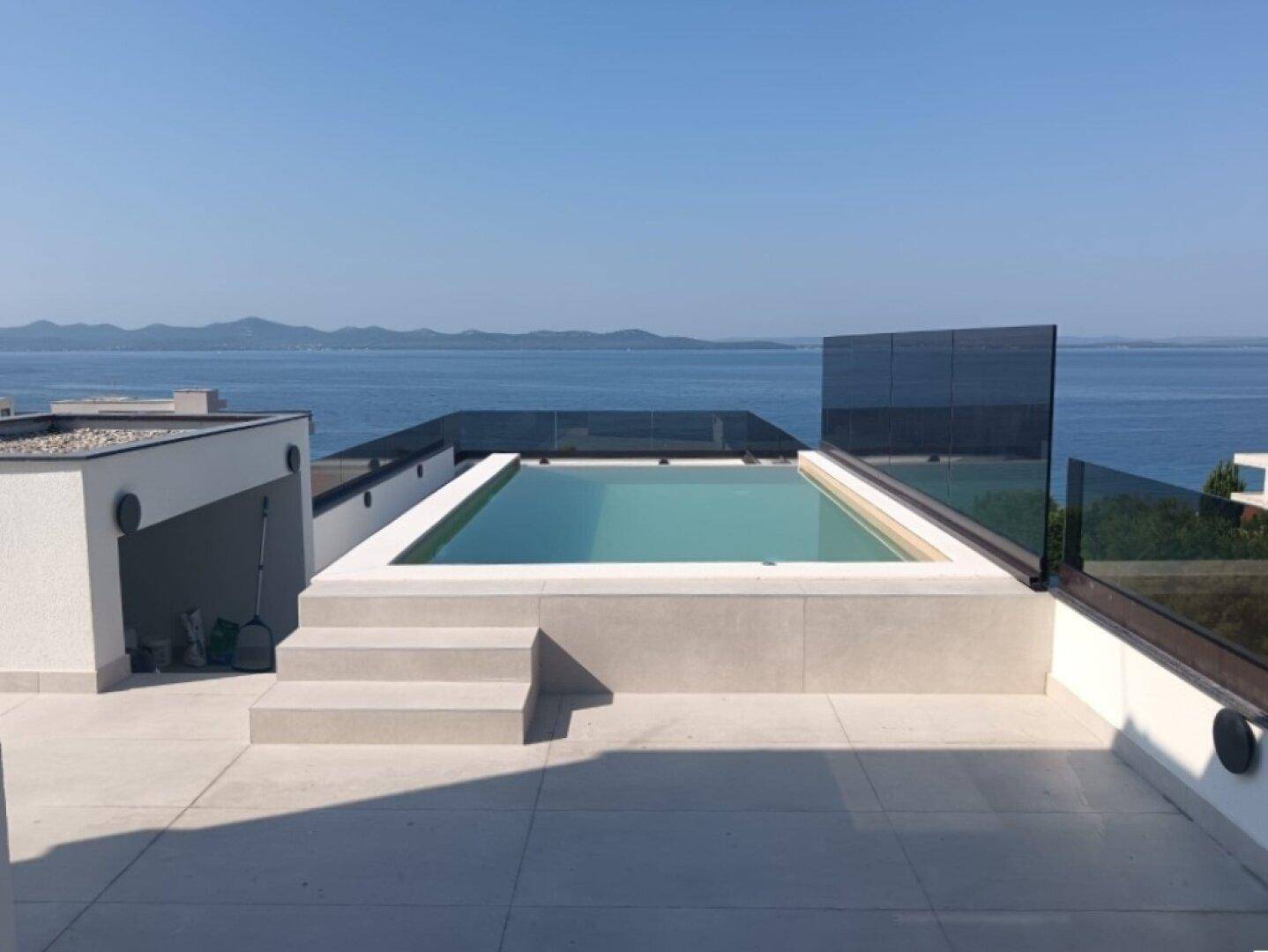 Dachterrasse mit Pool und weitem Meerblick unter blauem Himmel, perfekt zum Entspannen.