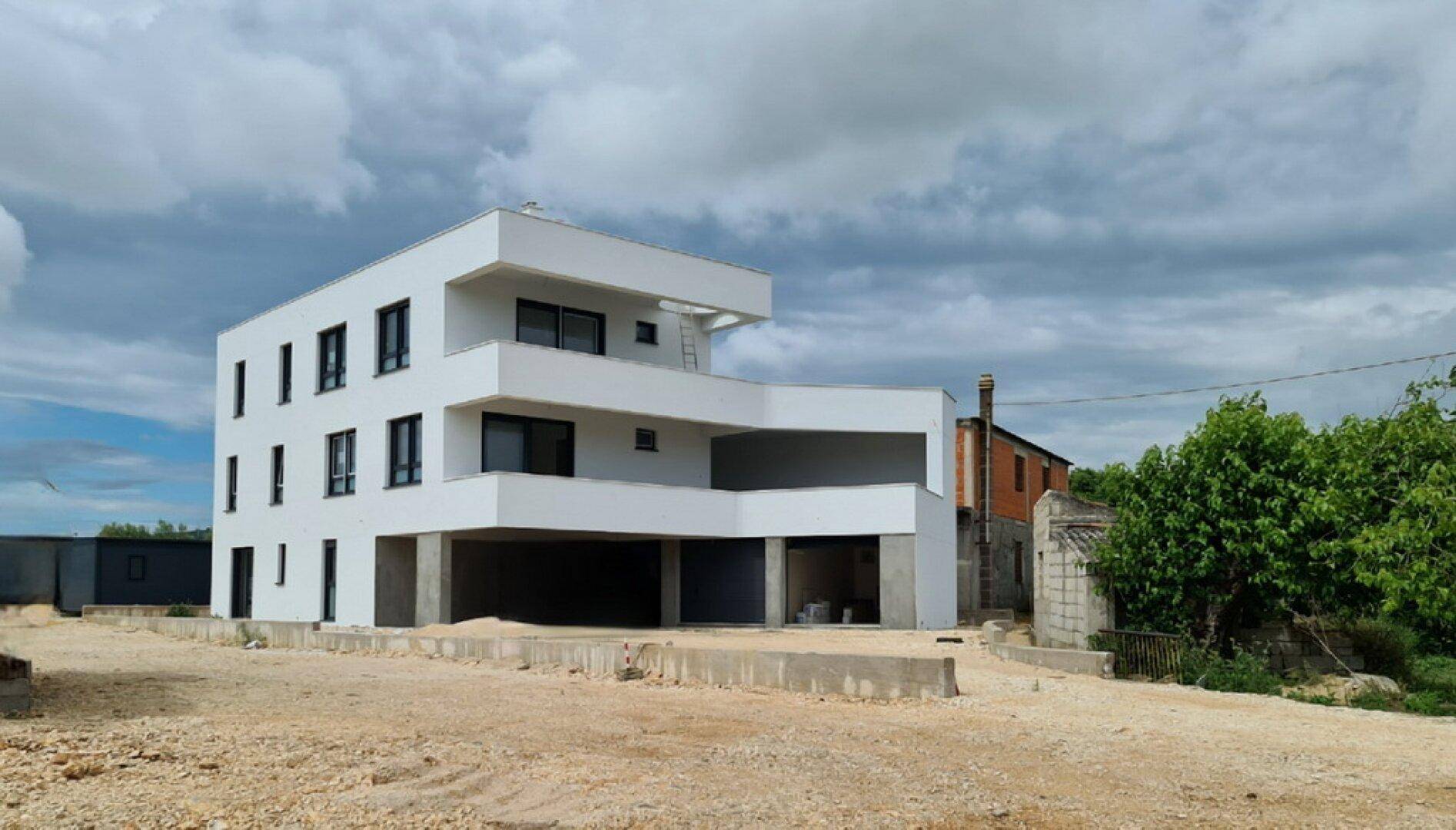 Modernes Gebäude im Bau mit weißen Fassaden, großen Fenstern und sichtbaren Balkonen.