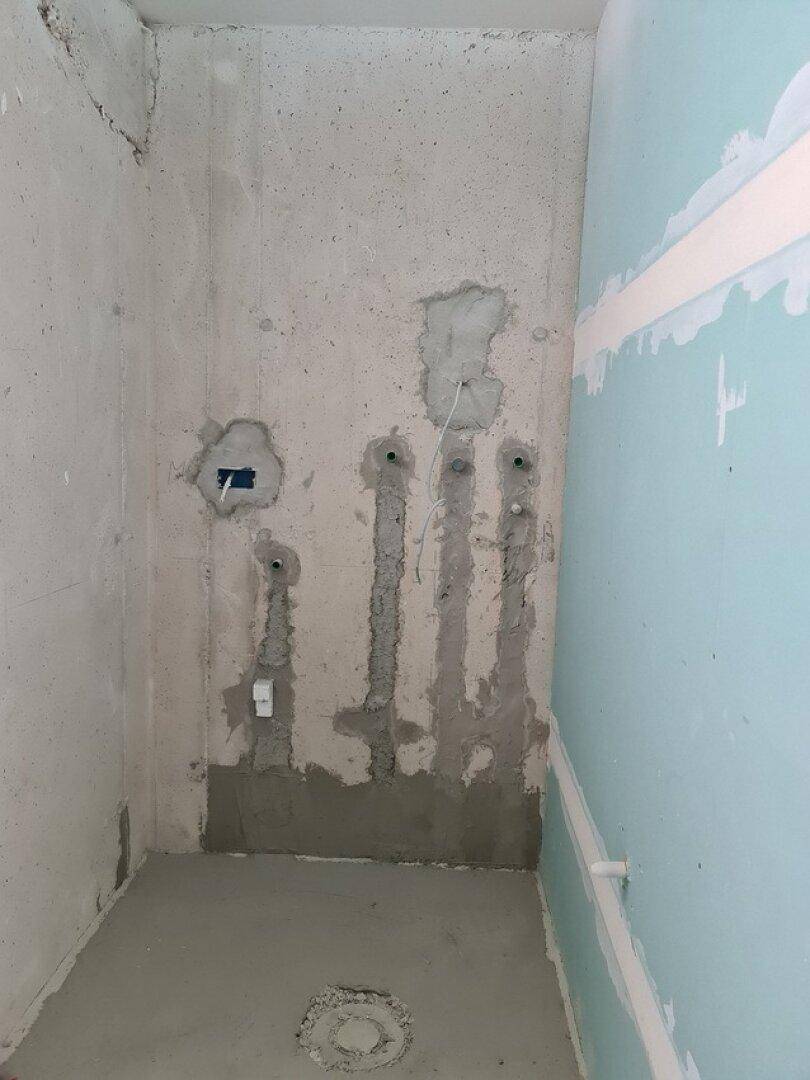 Unfertiges Badezimmer mit sichtbaren Rohrleitungen und teilweise verputzten Wänden.