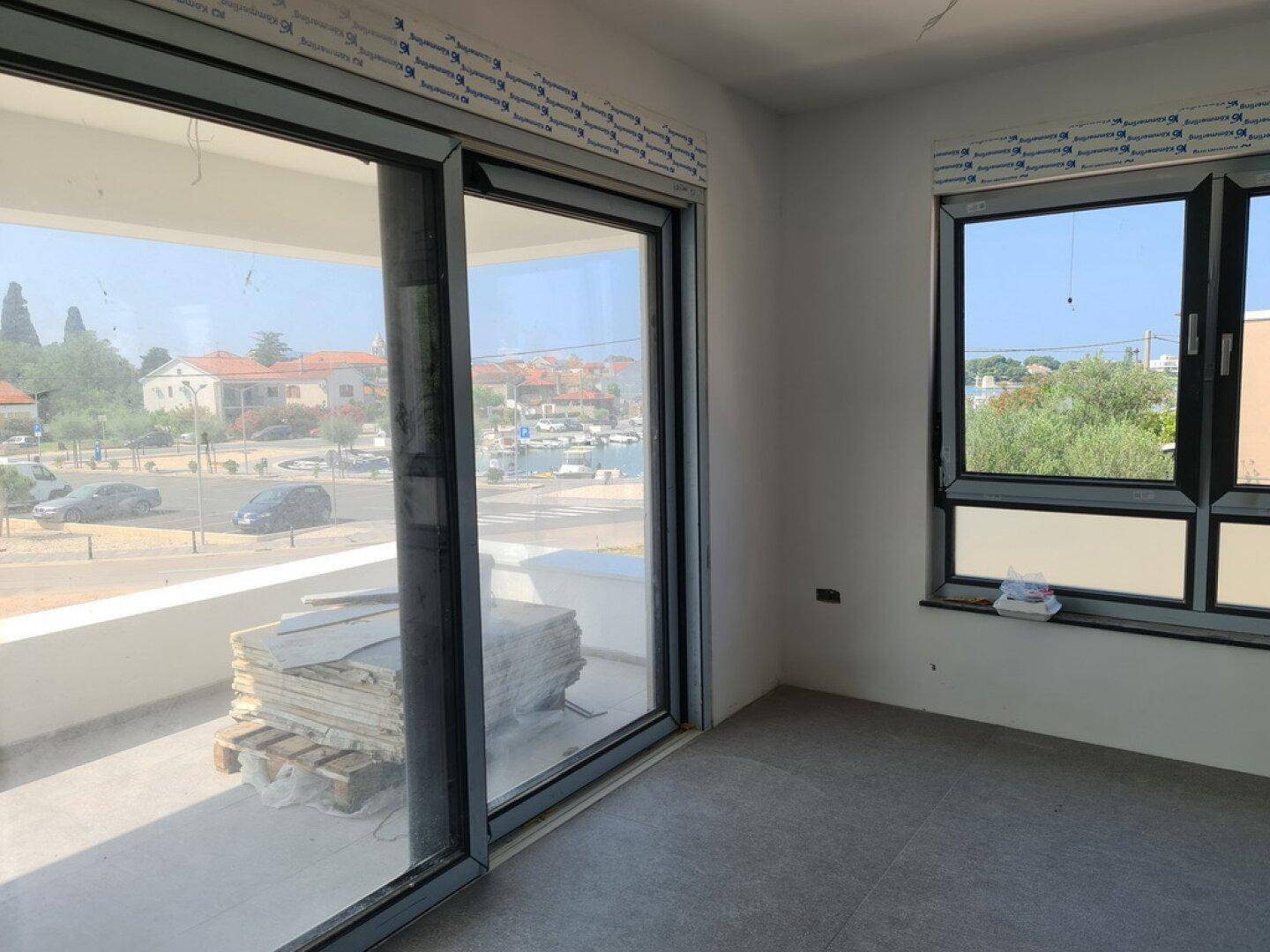 Heller, unfertiger Raum mit Schiebetür zum Balkon und Blick auf die Umgebung.