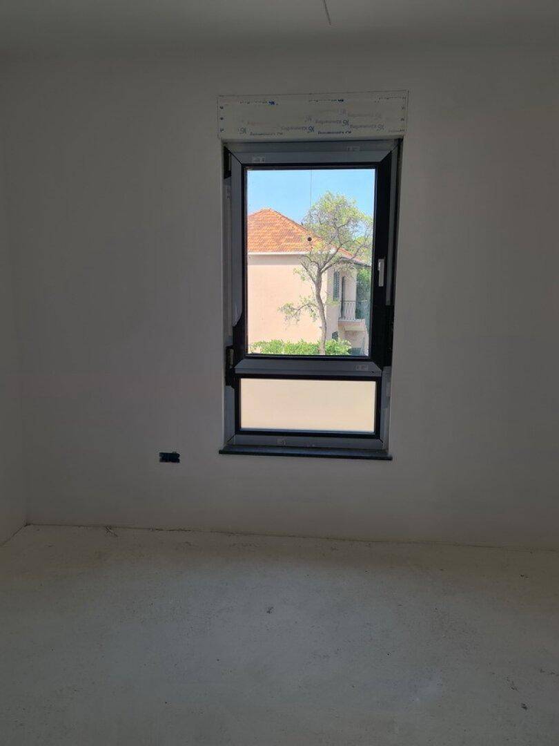 Unfertiges Zimmer mit weiß gestrichenen Wänden und einem Fenster mit Blick auf ein Nachbargebäude.