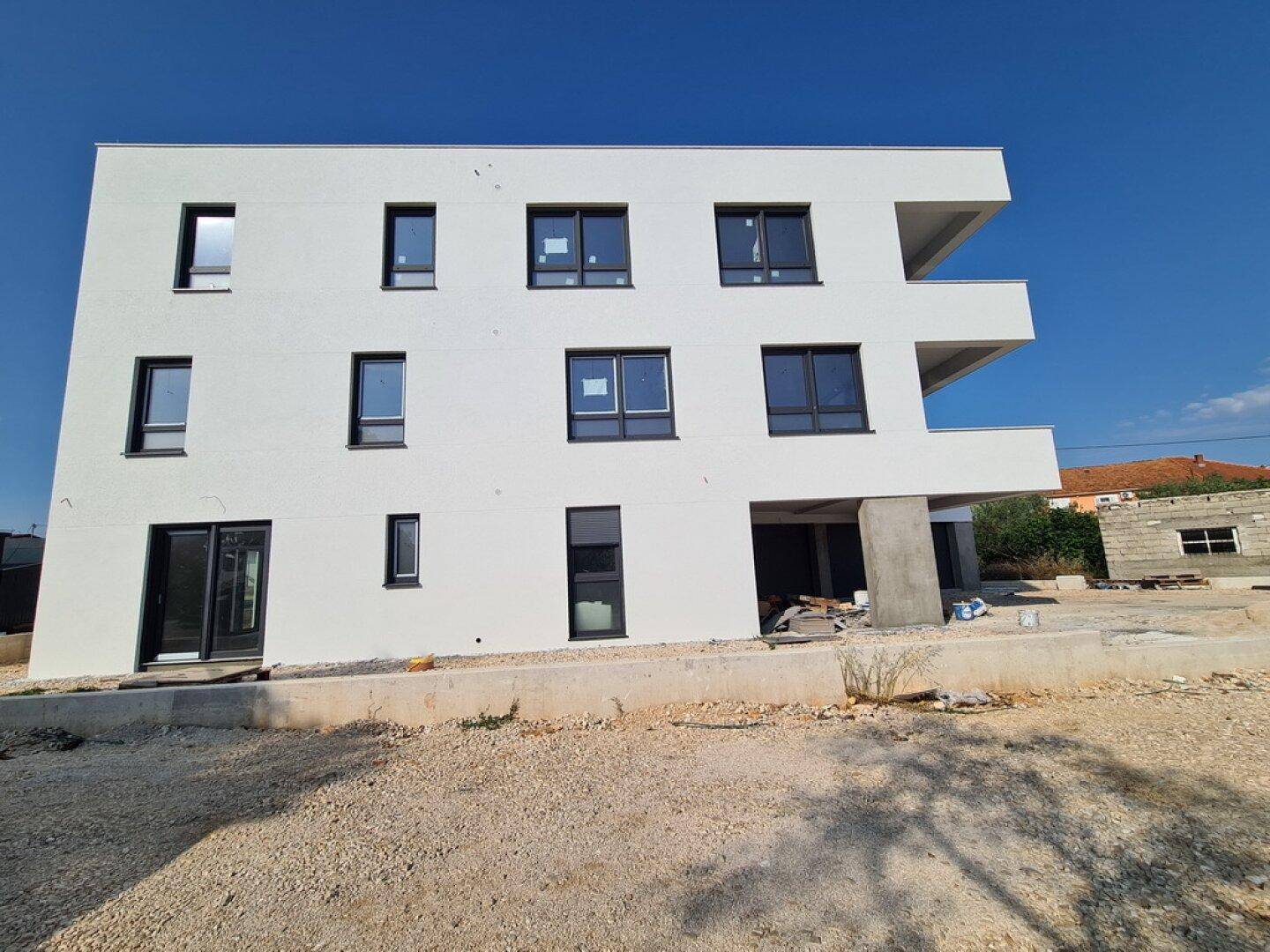 Seitenansicht eines modernen Neubaus mit weißen Wänden und dunklen Fensterrahmen.