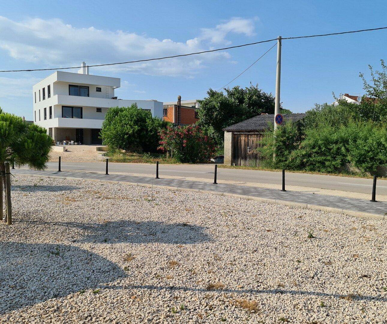 Blick auf ein modernes Gebäude in der Ferne, umgeben von einer Schotterfläche und einer Straße.