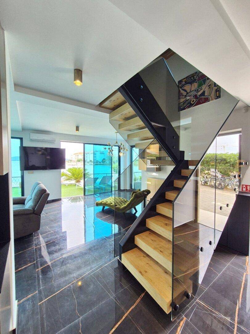 Offener Wohnbereich mit moderner Holztreppe, Glasgeländer und Blick auf den Außenbereich.