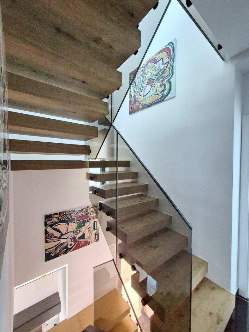 Elegante Holztreppe mit Glasgeländer und moderner Kunst an der Wand, die die Etagen verbindet.