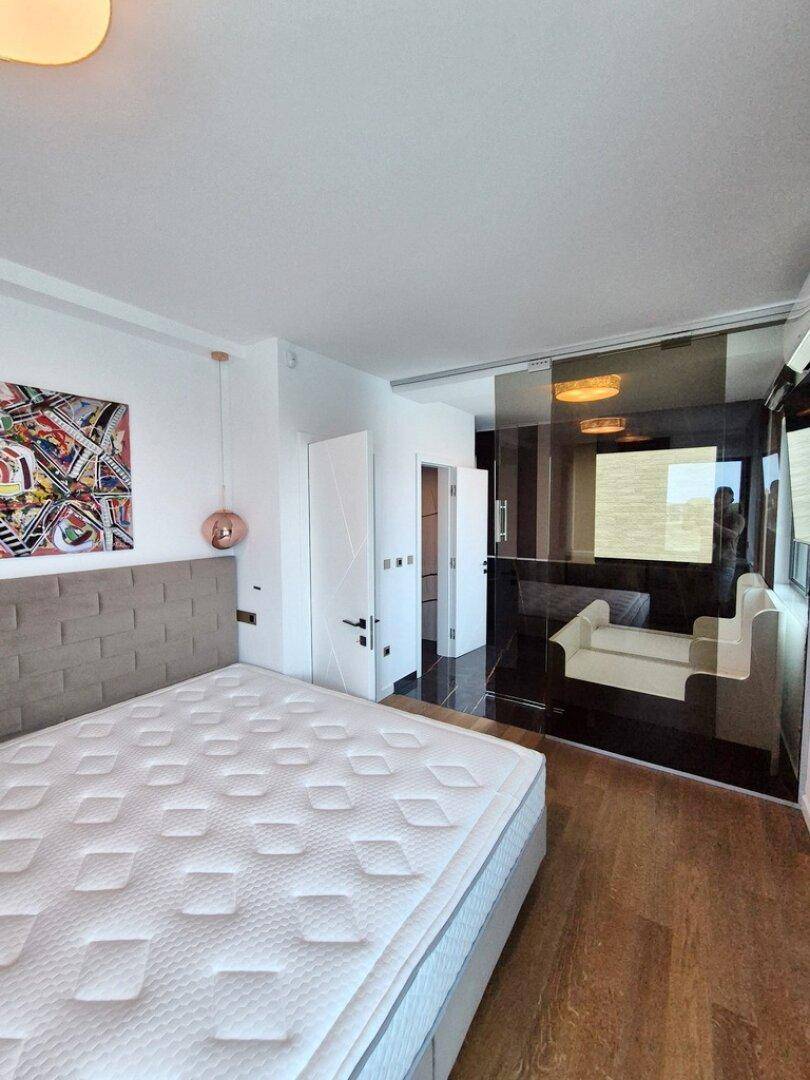 Modernes Schlafzimmer mit Holzboden, bequemen Bett und Zugang zu einem weiteren Bereich.
