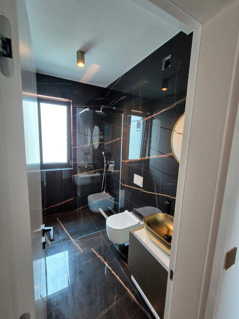 Luxuriöses Badezimmer mit dunklen Marmorfliesen, moderner Dusche und goldenem Waschbecken.
