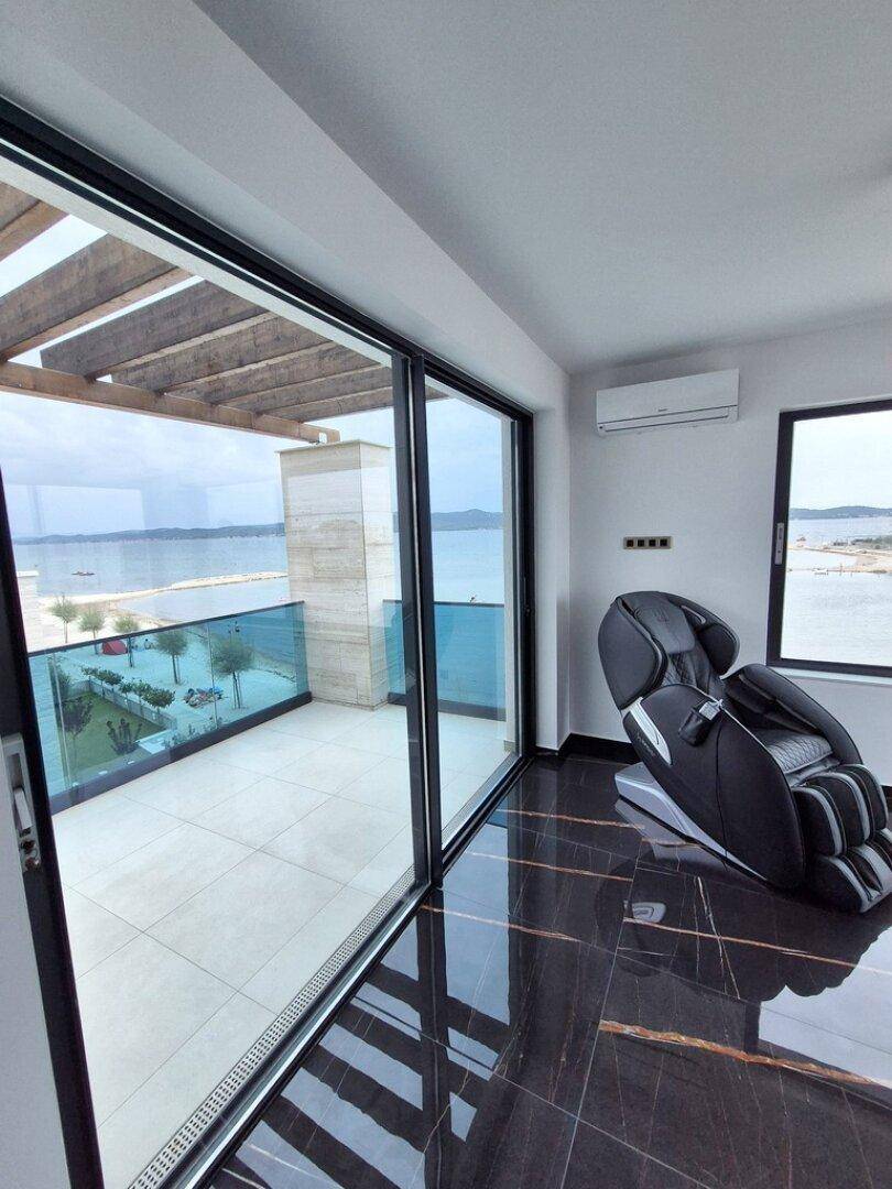 Heller Raum mit Massagesessel, großen Schiebetüren und direktem Zugang zur Dachterrasse mit Meerblick.