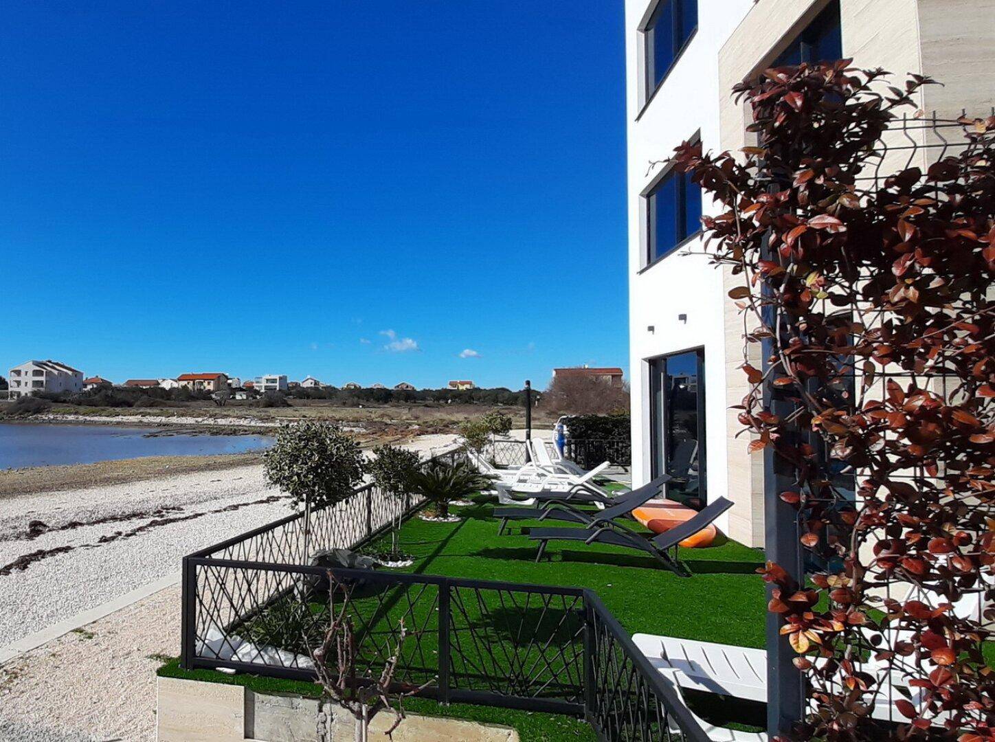 Gepflegter Gartenbereich mit Liegestühlen und Blick auf das Meer und die Küstenlandschaft.