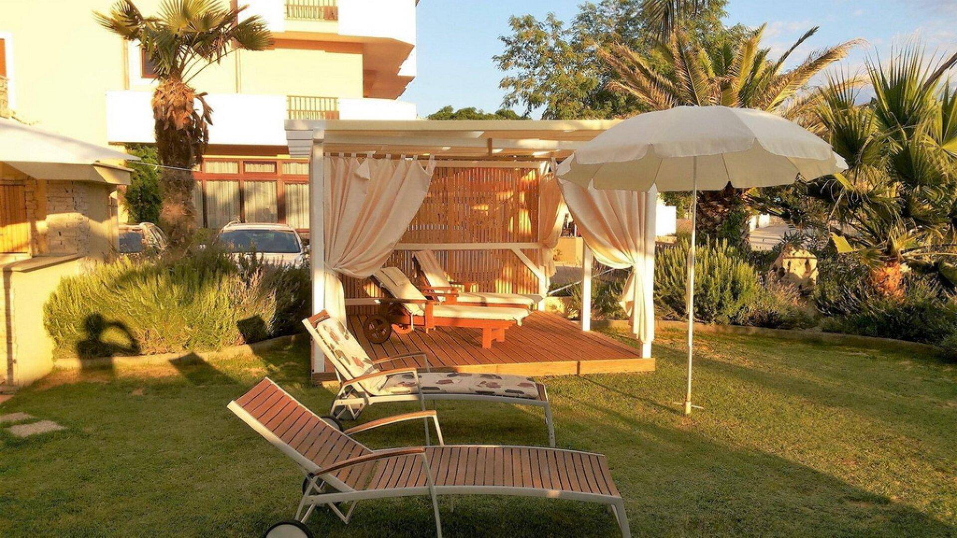Entspannender Gartenbereich mit Sonnenliegen, einer schattigen Cabana und üppiger mediterraner Bepflanzung.