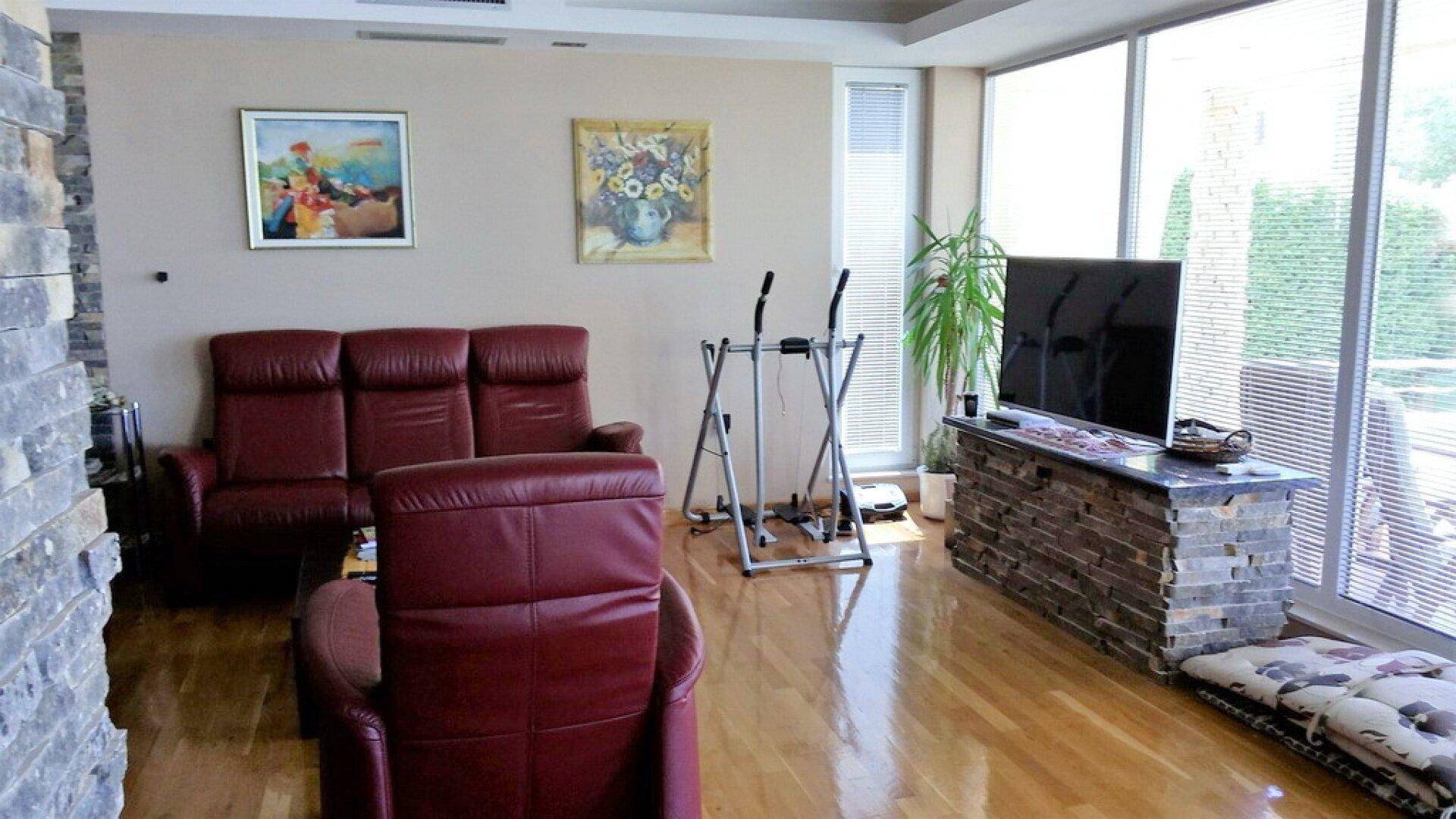 Geräumiges Wohnzimmer mit Holzboden, bequemen Ledersofas und großen Fenstern für natürliche Beleuchtung.