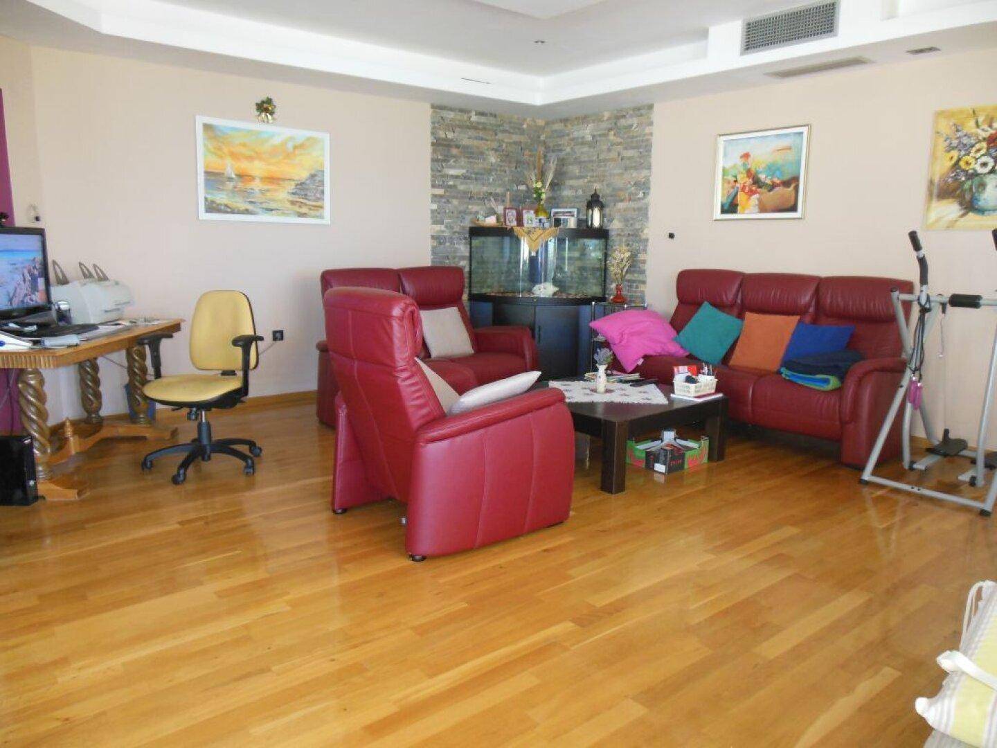 Helles Wohnzimmer mit Holzboden, roten Ledermöbeln und einem Aquarium als dekorativer Blickfang.