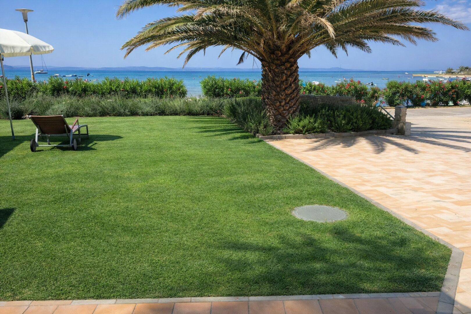 Gepflegte Rasenfläche im Garten mit gepflastertem Bereich und Blick auf das weite Meer.