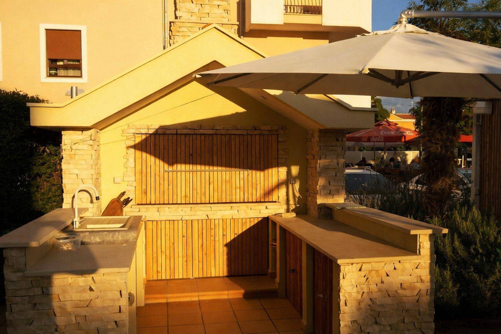 Gut ausgestattete Außenküche mit Grillbereich, Spüle und Arbeitsflächen aus Naturstein und Holzverkleidung.