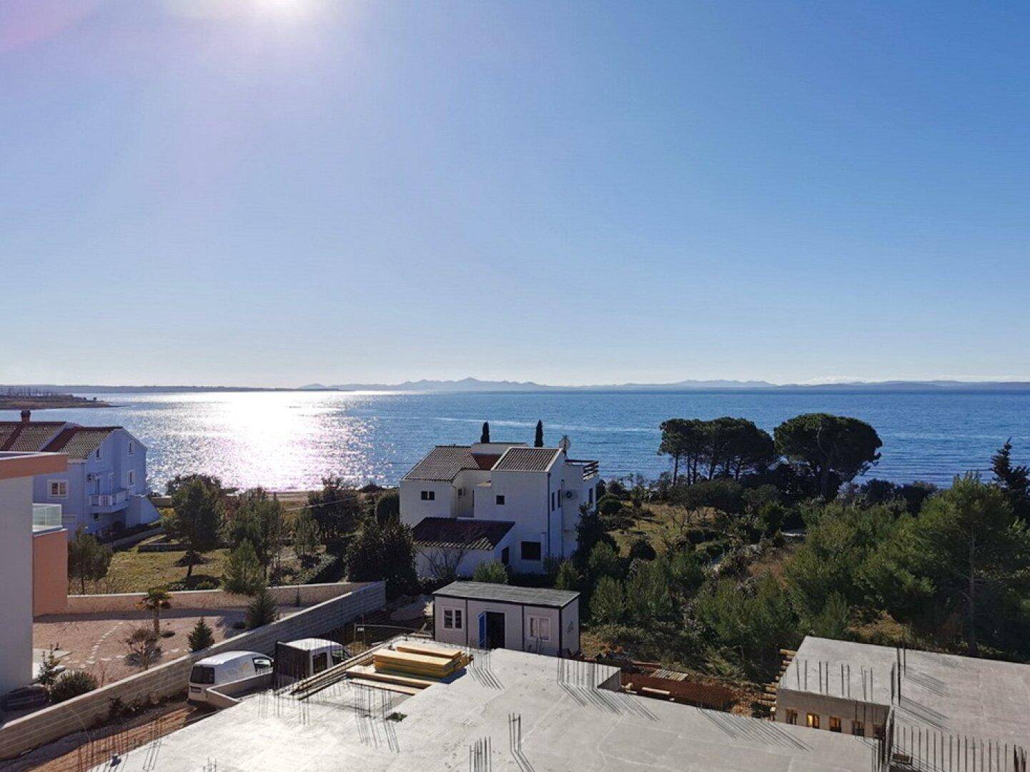 Panoramablick auf das glitzernde Meer und die Küstenlandschaft unter strahlend blauem Himmel.
