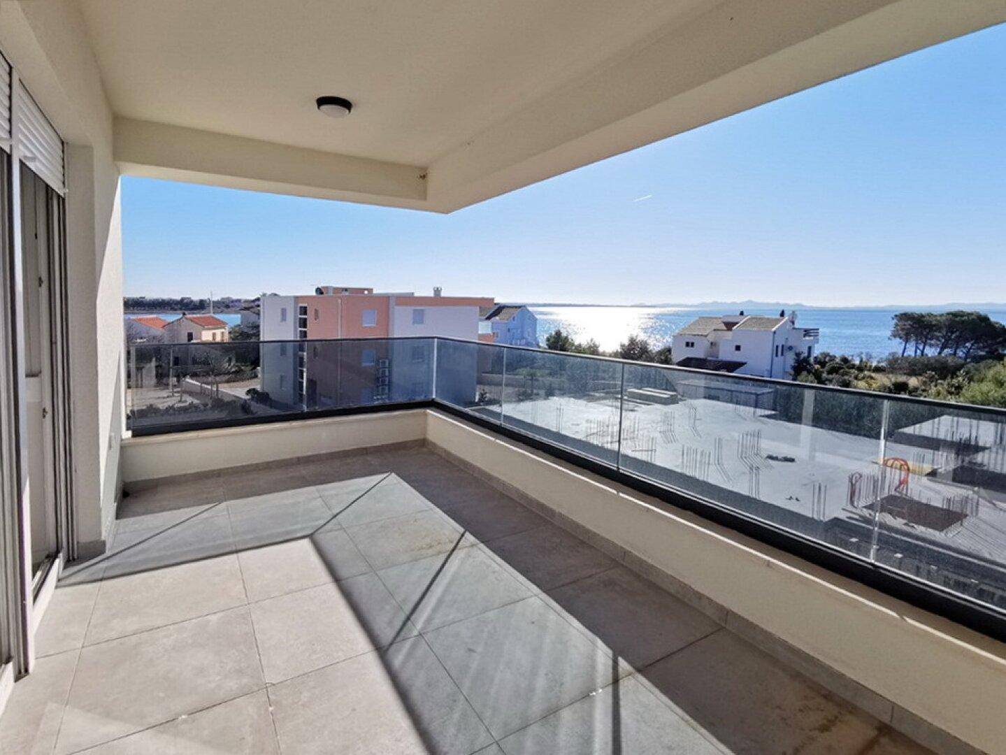 Geräumiger Balkon mit Glasgeländer und weitem Meerblick unter blauem Himmel, ideal zum Entspannen.