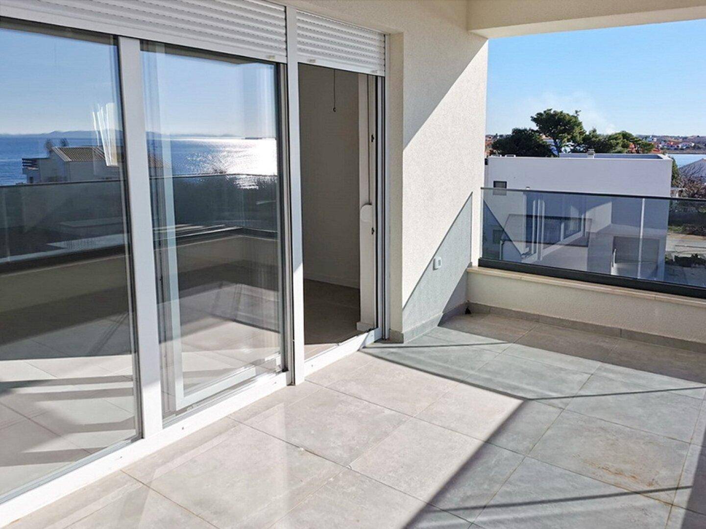 Heller Balkon mit großen Schiebetüren und Glasgeländer, bietet einen schönen Meerblick.
