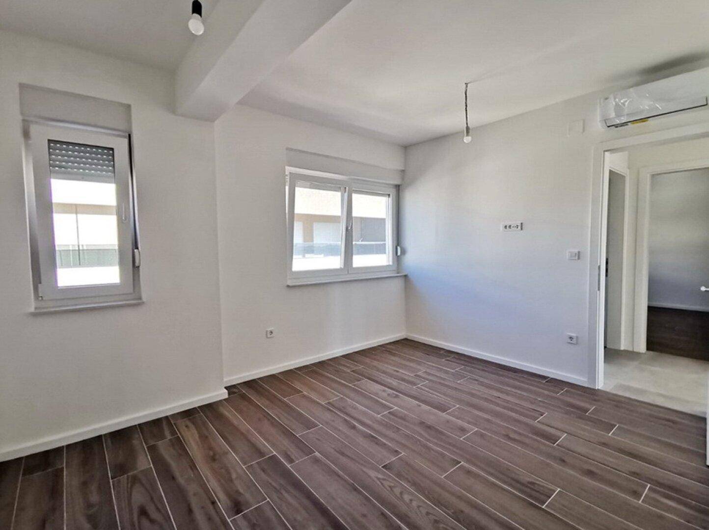 Helles Schlafzimmer mit Holzoptik-Fliesenboden und Fenster mit Rollladen, bereit zum Einrichten.