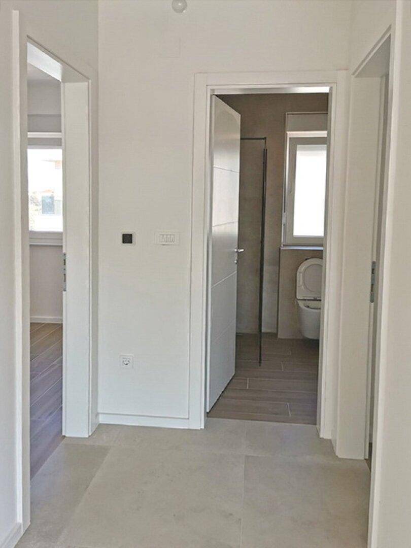 Heller Flur mit Fliesenboden, der zu einem modernen Badezimmer führt, in neuwertigem Zustand.