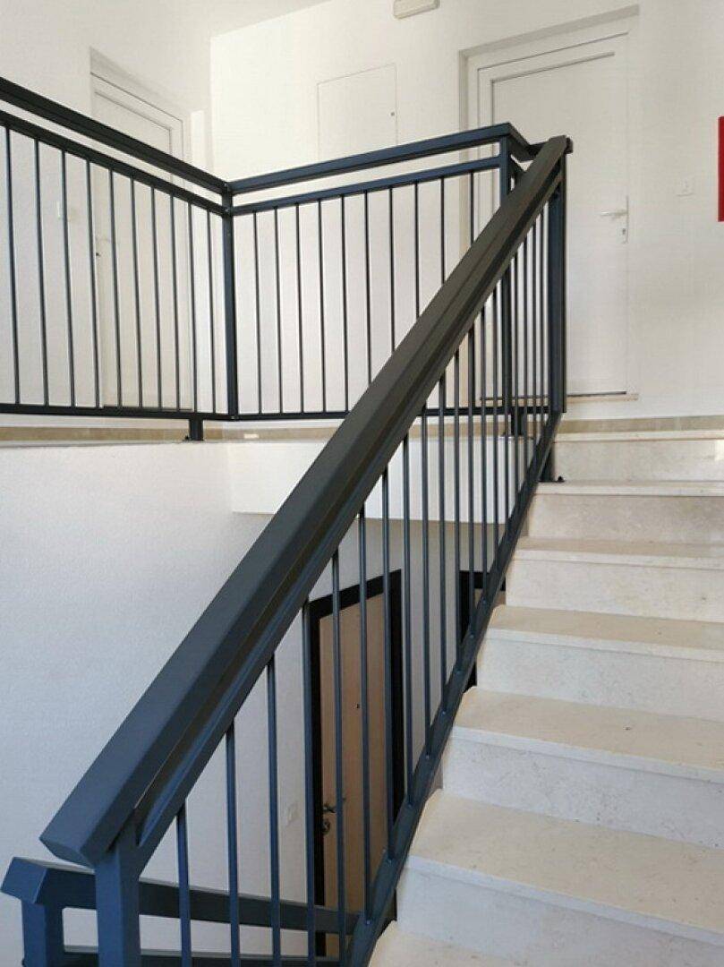 Heller Treppenaufgang mit modernem Metallgeländer und hellen Fliesenstufen in einem Mehrfamilienhaus.
