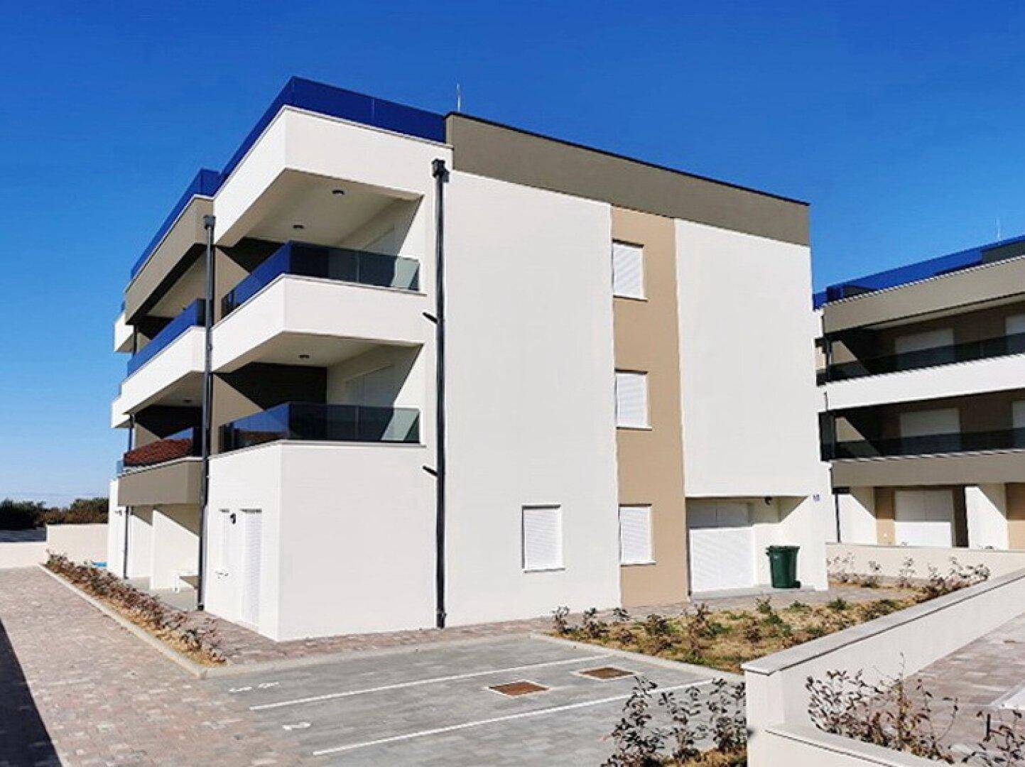 Modernes Mehrfamilienhaus mit Balkonen und Flachdach in sonniger Lage, umgeben von gepflegten Außenanlagen.