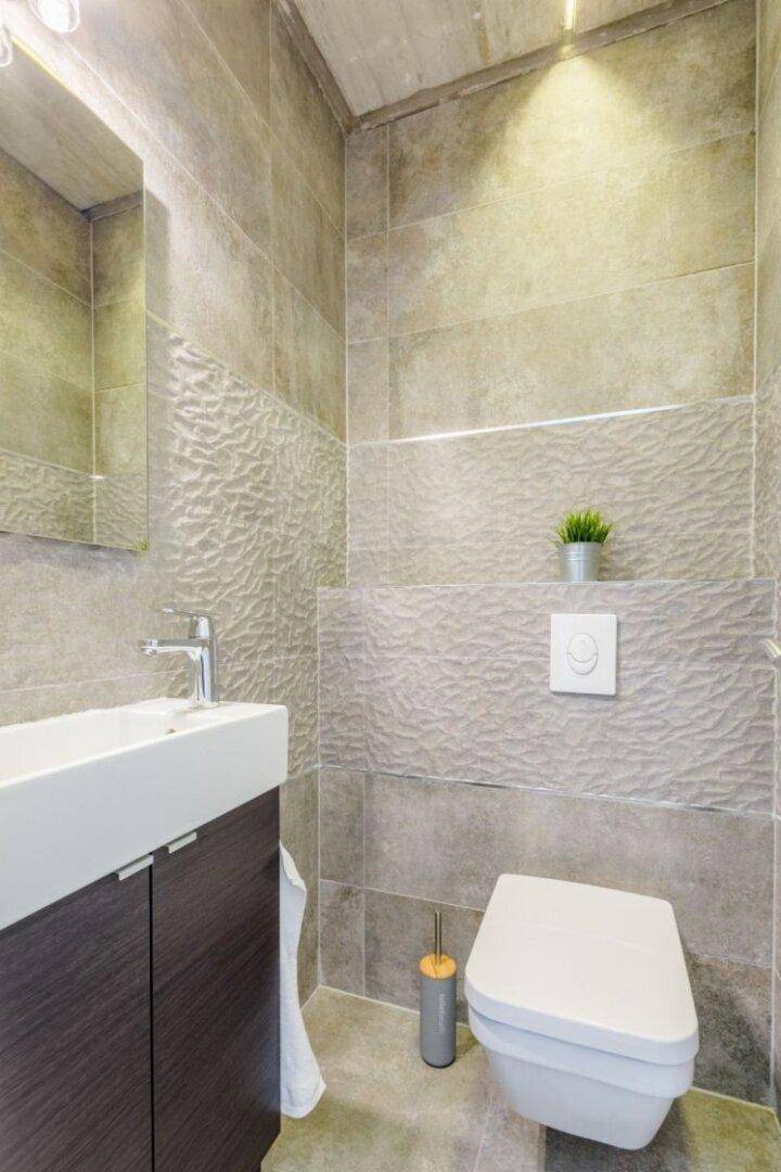 Modernes Gäste-WC mit grauen Fliesen, wandhängendem WC und kleinem Waschbecken.
