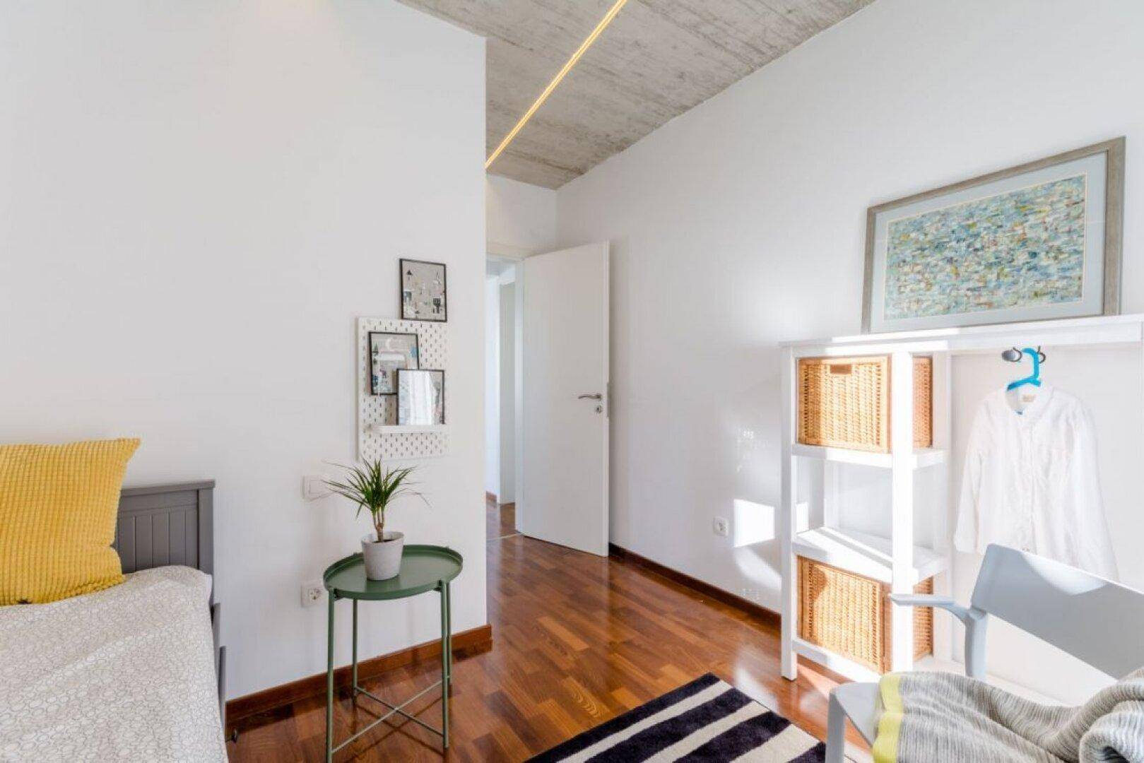 Helles Schlafzimmer mit Holzboden, moderner Einrichtung und sichtbarer Betondecke.