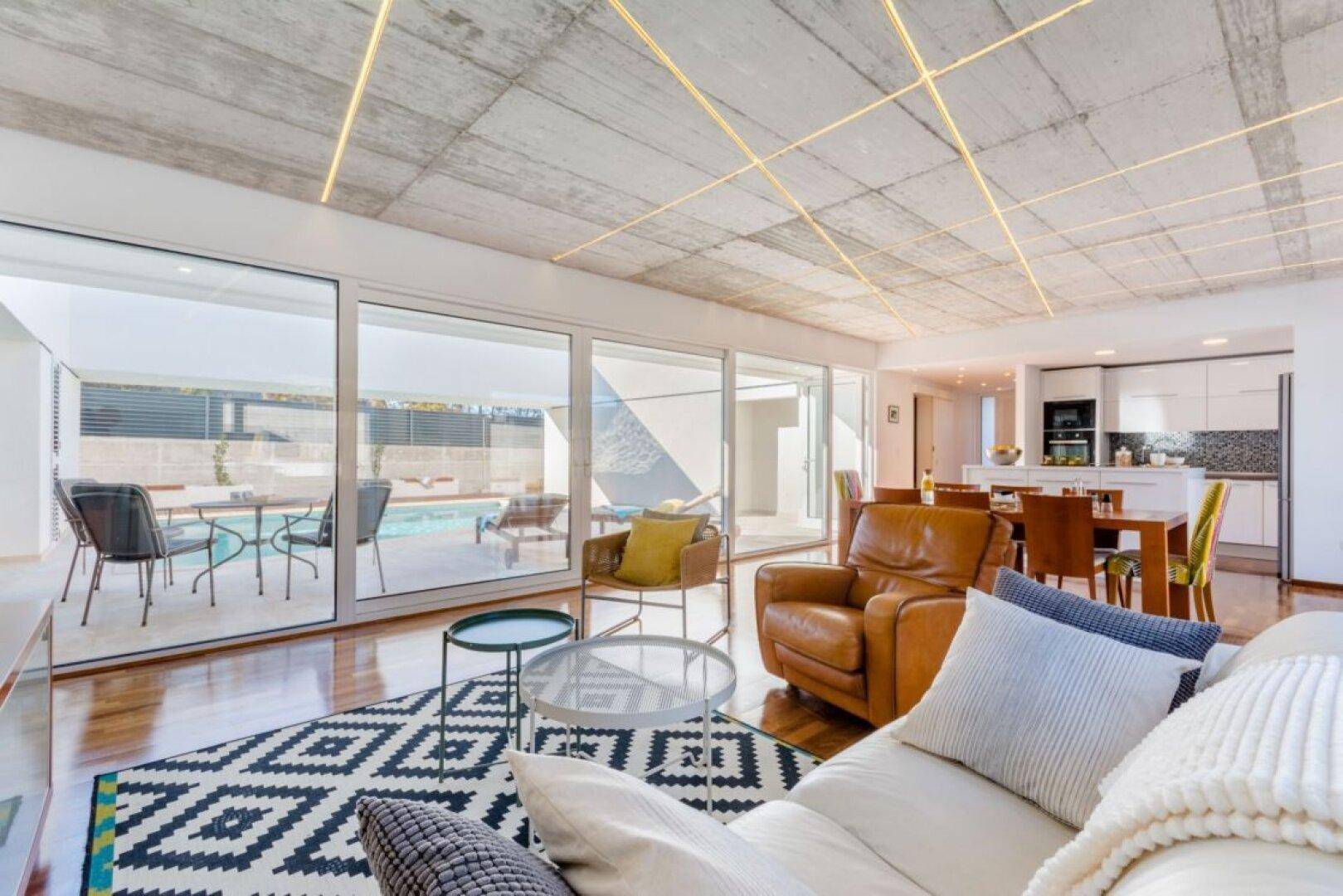 Offener Wohnbereich mit Blick auf die moderne Küche und den Pool durch große Fenster.