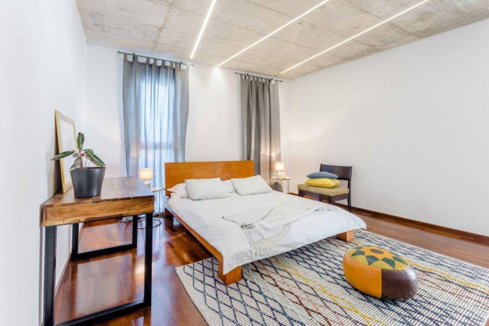 Gemütliches Schlafzimmer mit Holzboden, minimalistischer Einrichtung und sichtbarer Betondecke.