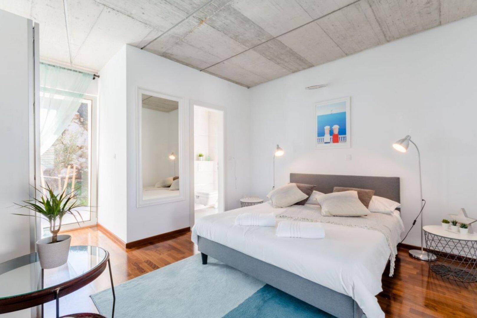 Modernes Schlafzimmer mit Holzboden, großem Bett und Zugang zu einem weiteren Raum.