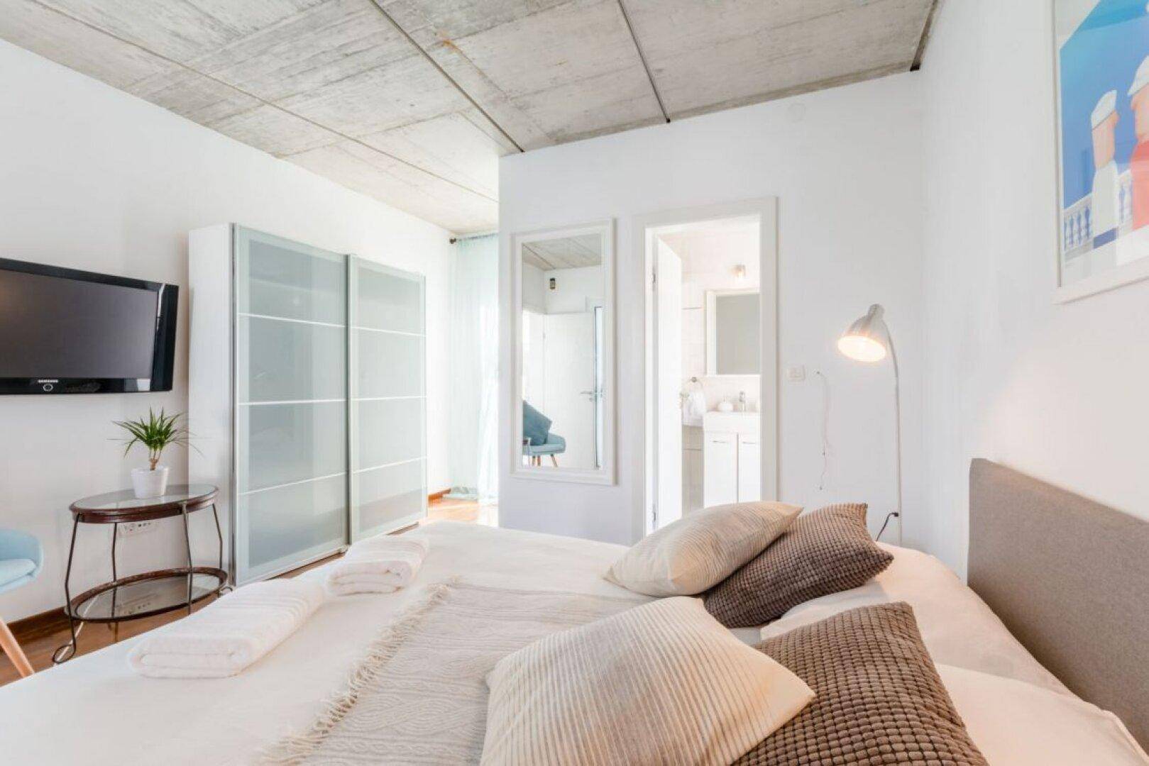Schlafzimmer mit Fernseher, Schiebetürenschrank und Holzboden, hell und modern eingerichtet.