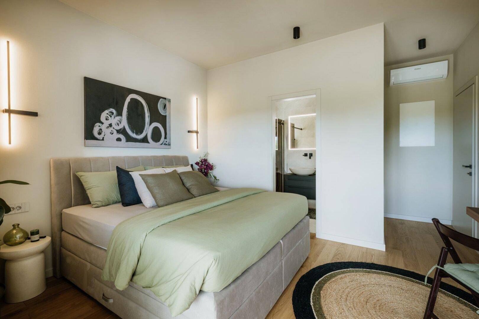 Helles Schlafzimmer mit modernem Bett, Kunstwerk und Zugang zu einem eleganten Badezimmer.
