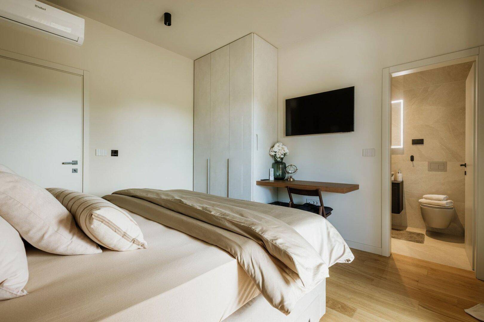 Schlafzimmer mit Doppelbett, Einbauschrank und direktem Zugang zu einem modernen Badezimmer.