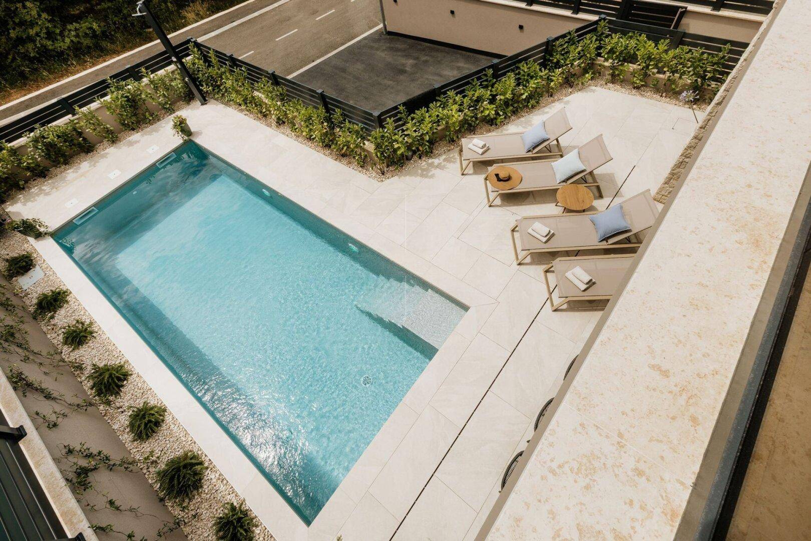 Ansicht von oben auf den privaten Poolbereich mit Sonnenliegen und heller Fliesenterrasse.