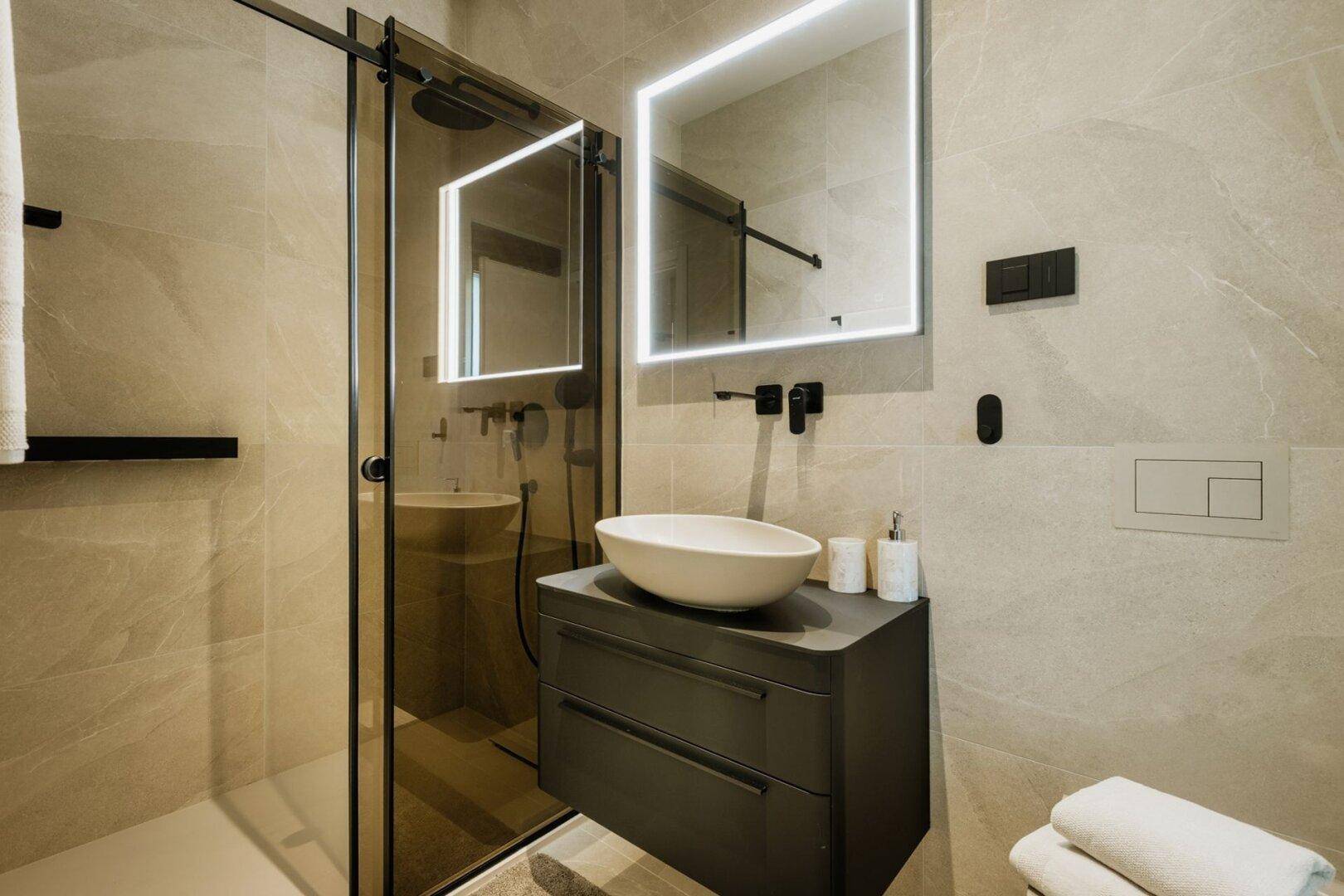 Modernes Badezimmer mit begehbarer Dusche, stilvollem Waschtisch und beleuchtetem Spiegel.