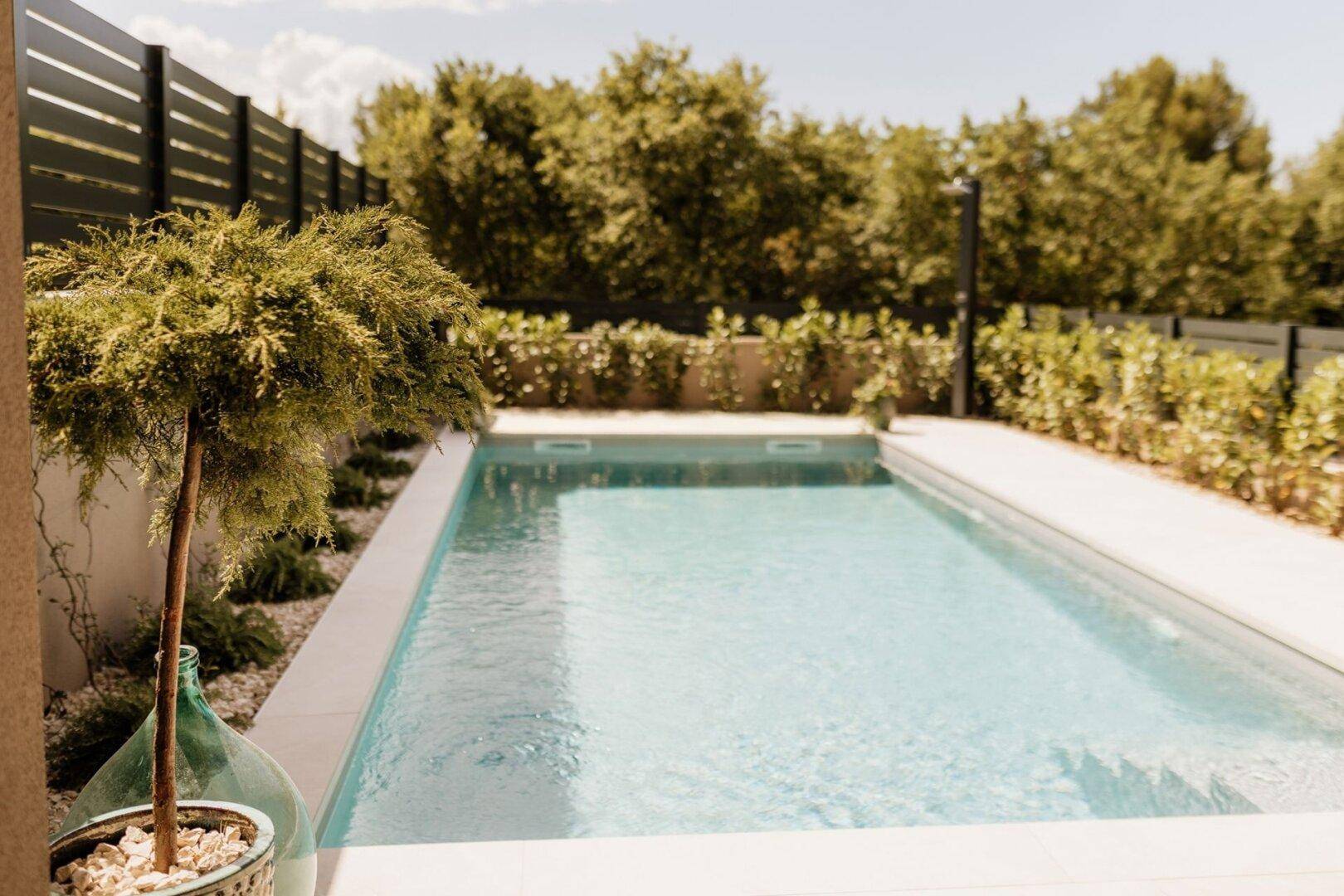 Privater Swimmingpool umgeben von grüner Bepflanzung und einer modernen Zaunanlage.
